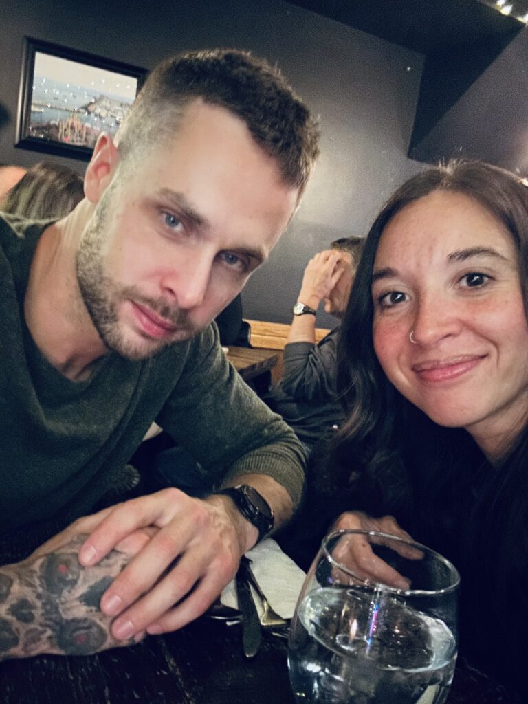 Couple smiling at the camera while seated at a cozy restaurant table on Valentine's Day.