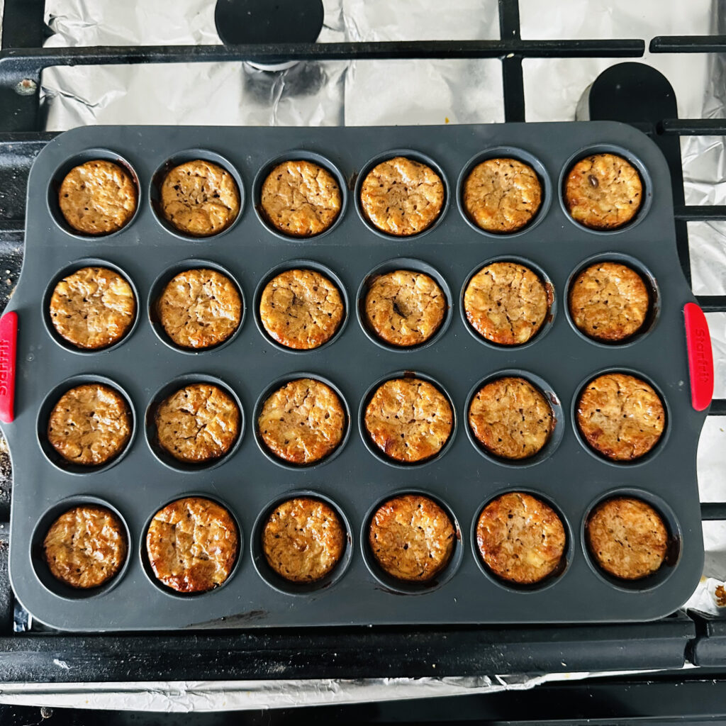 Freshly baked mini protein muffins in a silicone tray, golden brown and cooling on a stovetop.